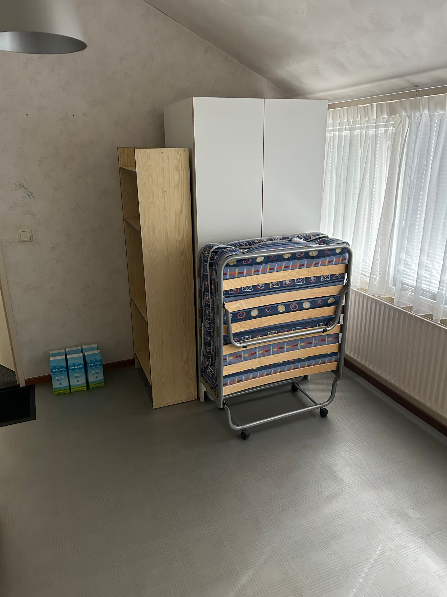 Slaapkamer met rolbed, plank en spullen vóór de ontruiming door Sens